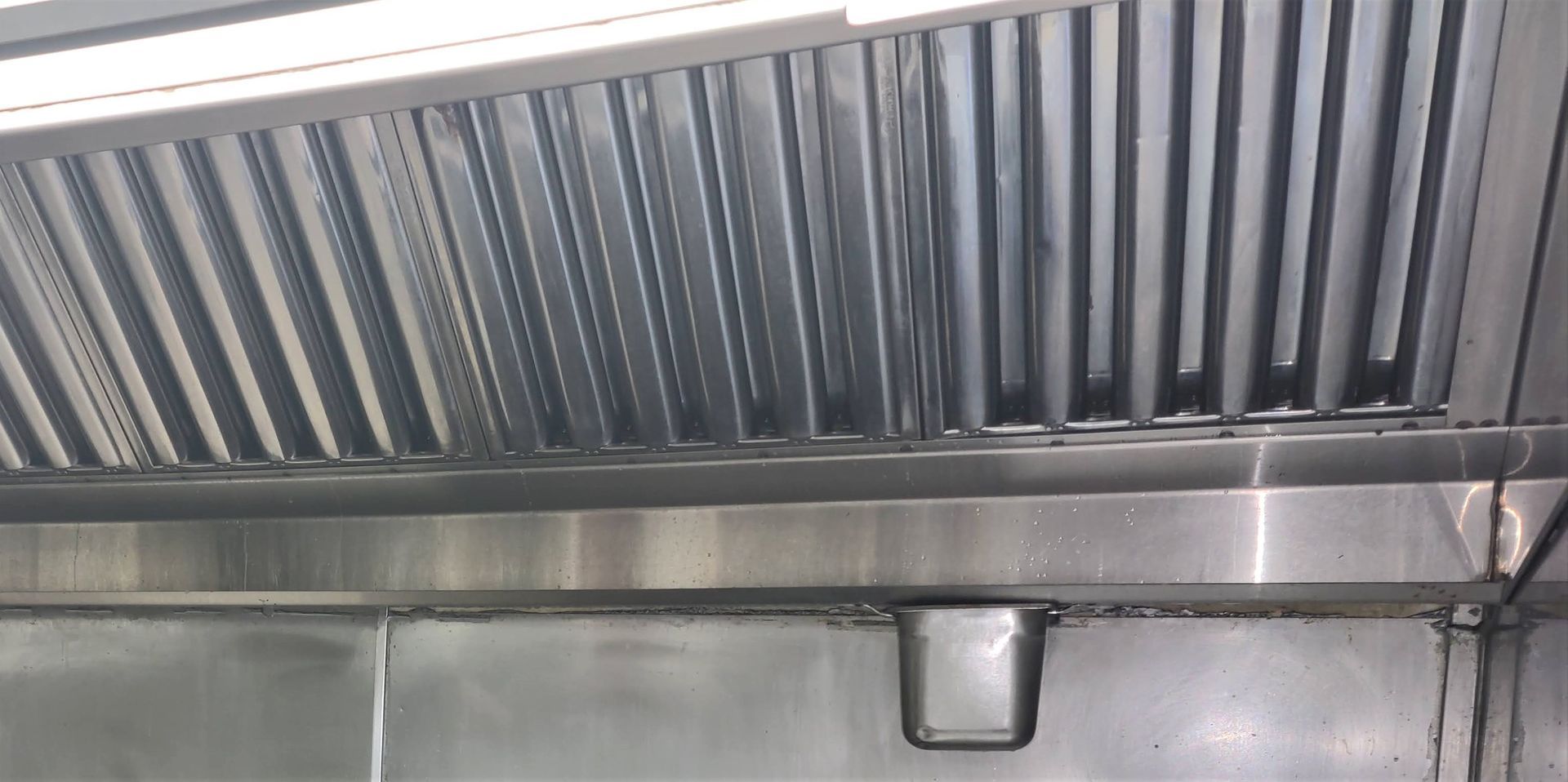 A stainless steel hood is hanging from the ceiling of a kitchen.