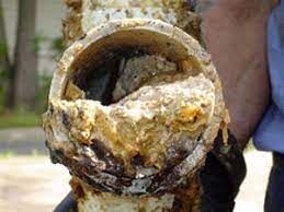 A person is holding a very rusty pipe with a hole in it.