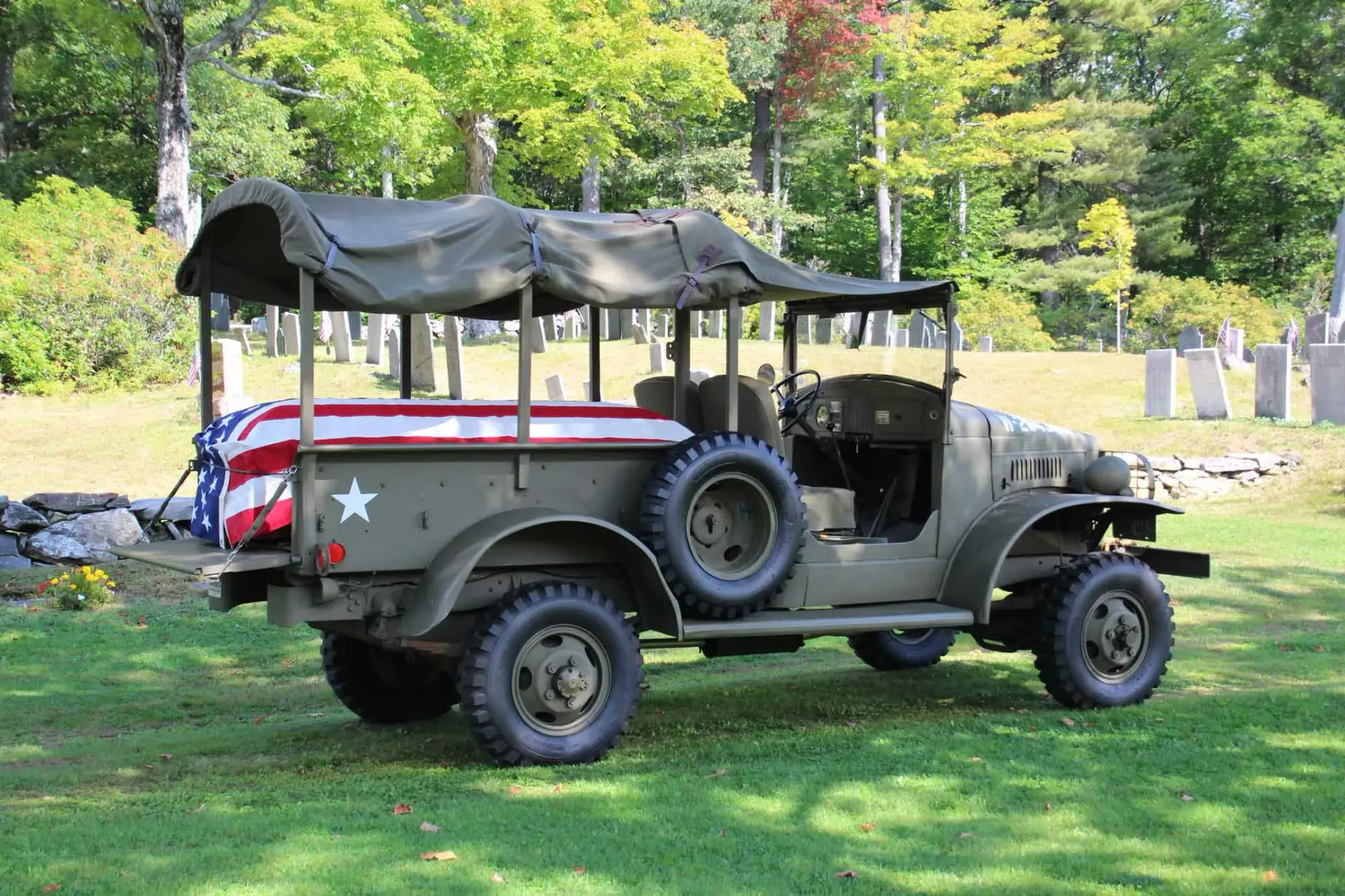 A military vehicle with an american flag on the back is parked in a grassy field.