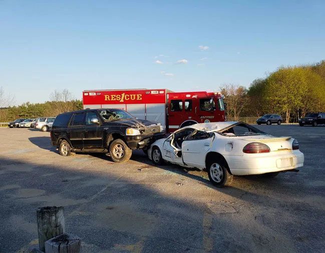 A car accident in a parking lot with a rescue truck in the background.
