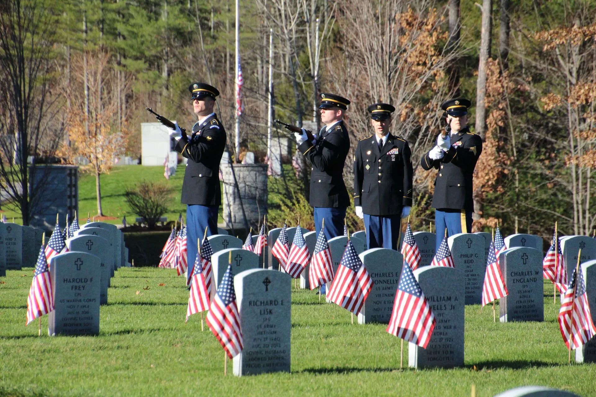 A group of soldiers are standing in front of a cemetery with american flags.