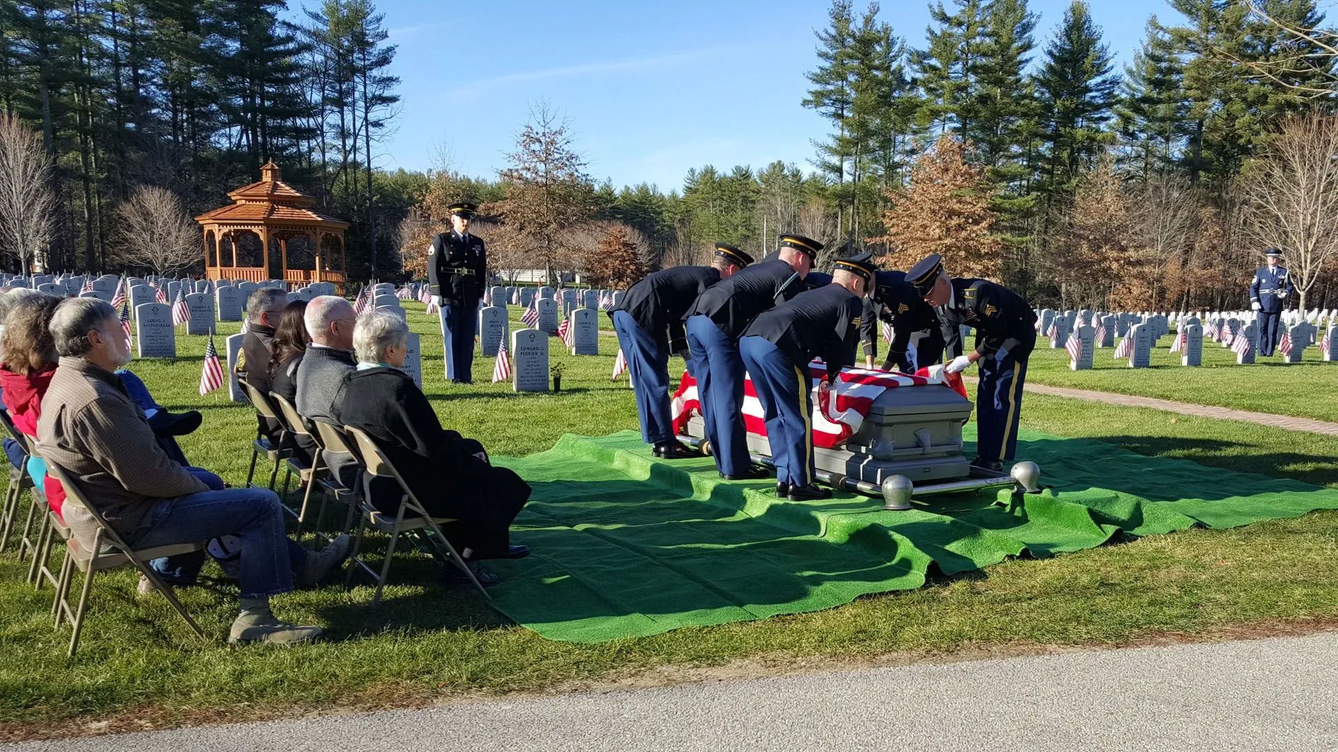 A group of people are standing around a coffin in a cemetery.