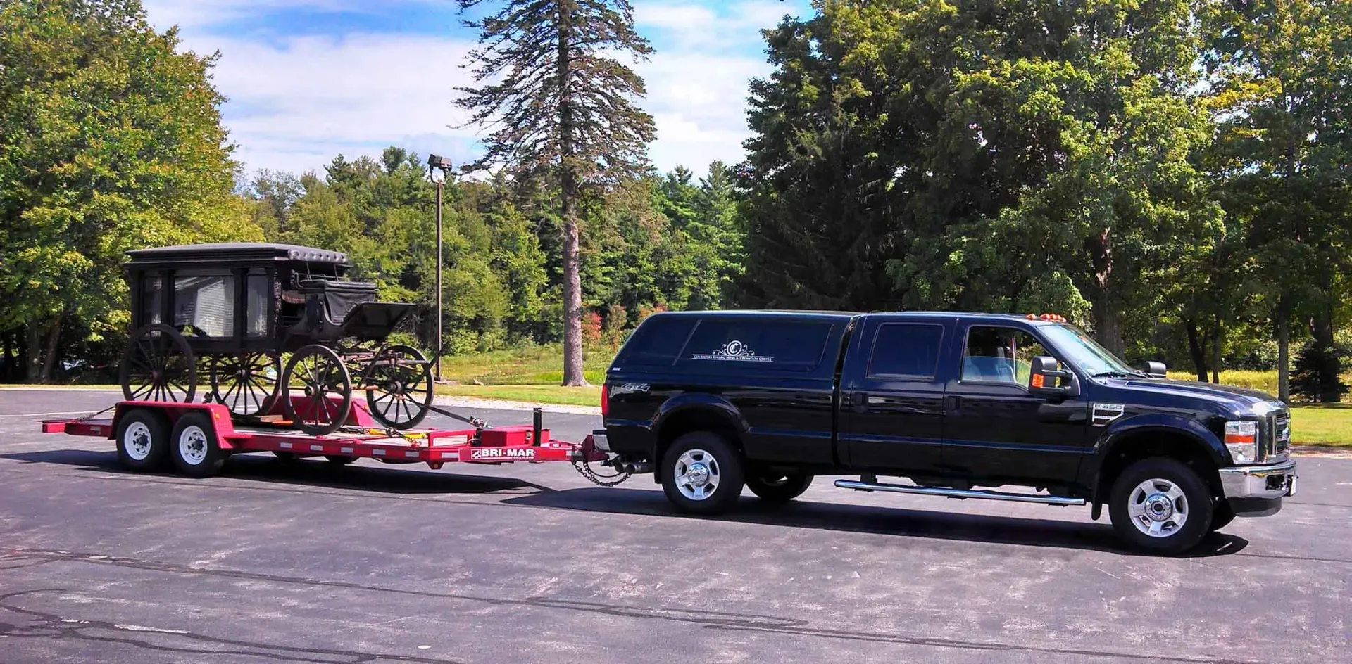 A black truck is towing a horse drawn carriage in a parking lot.