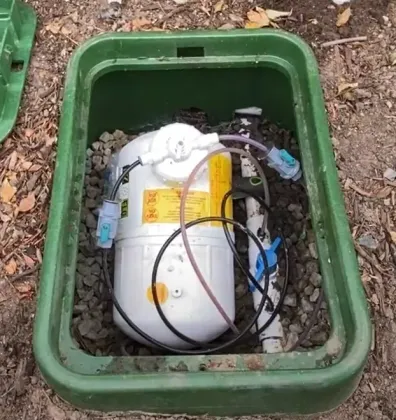 White water filtration unit in a green utility box, with cables and gravel around it.