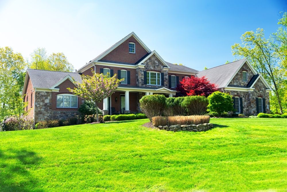 Large brick house with a manicured green lawn, front porch, and blue sky on a sunny day