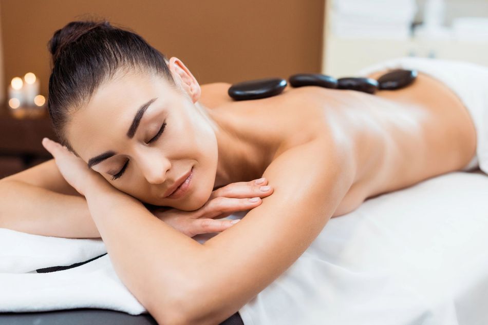Woman receiving a hot stone massage while lying face down on a spa table