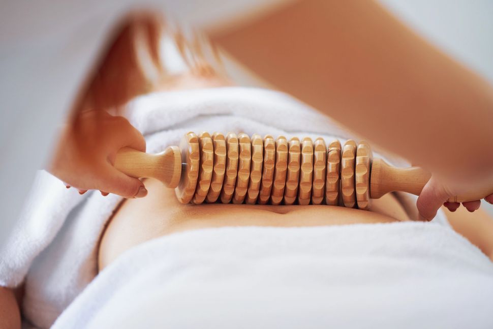 Hands holding a wooden massage roller on a person’s back, used on a white towel