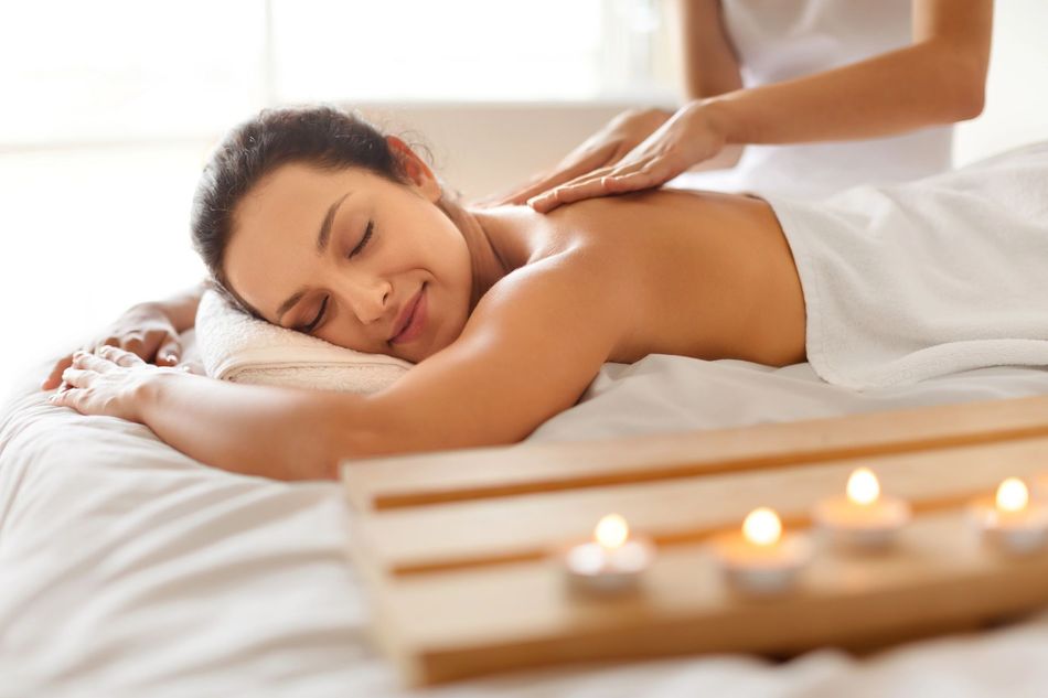 Person receiving a relaxing back massage with candles on a spa table