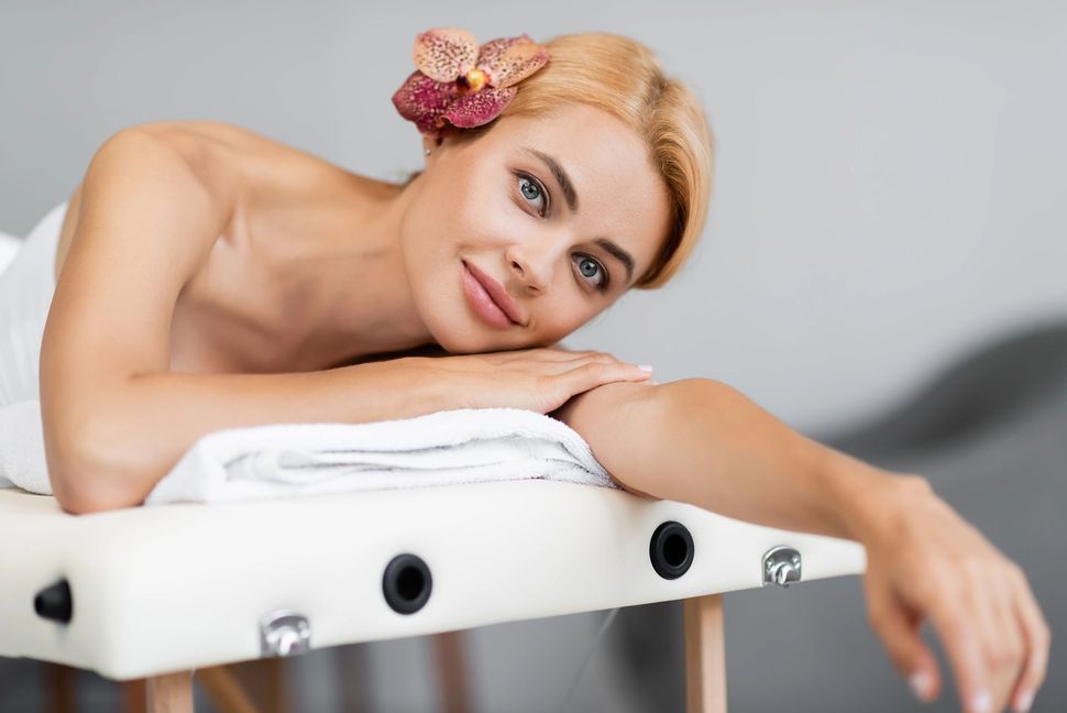 Blonde woman lying on a white massage table, resting her head on folded towels