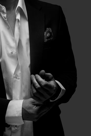 Homme en costume sombre ajustant ses poignets et ses poignets, chemise blanche et pochette de costume, sur fond sombre