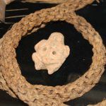 A close up of a crocheted necklace with a skull in the middle.