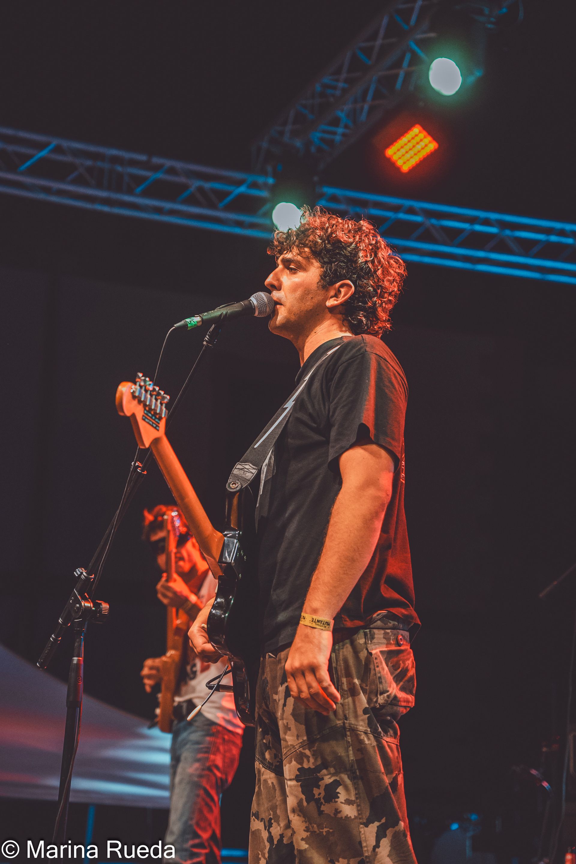 Un hombre canta en un micrófono mientras toca una guitarra en el escenario.