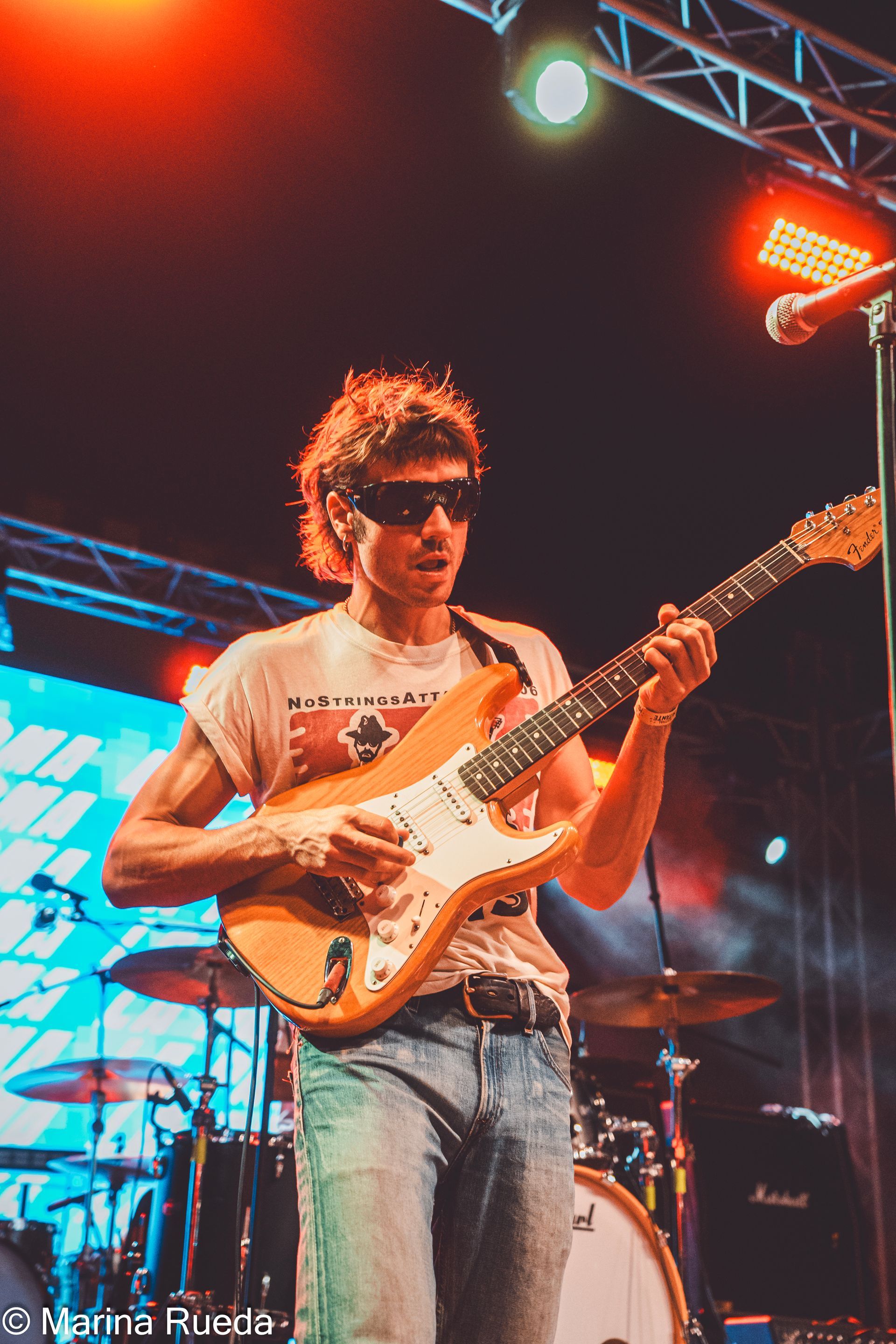 Un hombre que lleva gafas de sol está tocando una guitarra en un escenario.