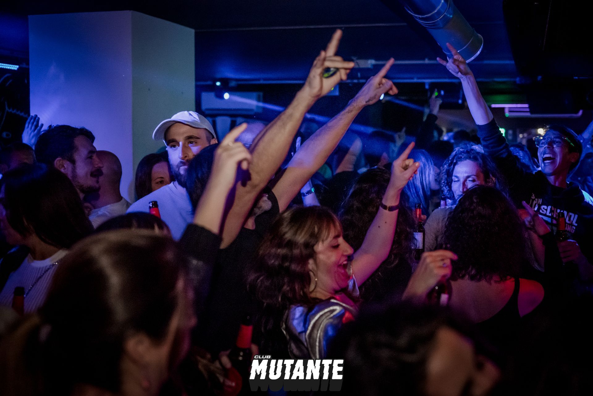Una multitud de personas baila en un club con las manos en el aire.