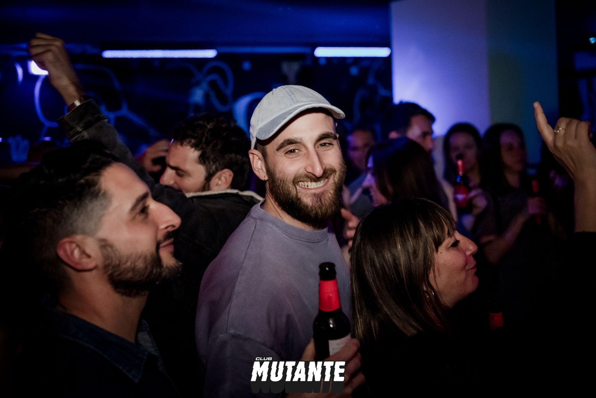 Un hombre sostiene una botella de cerveza entre una multitud de personas en una fiesta.