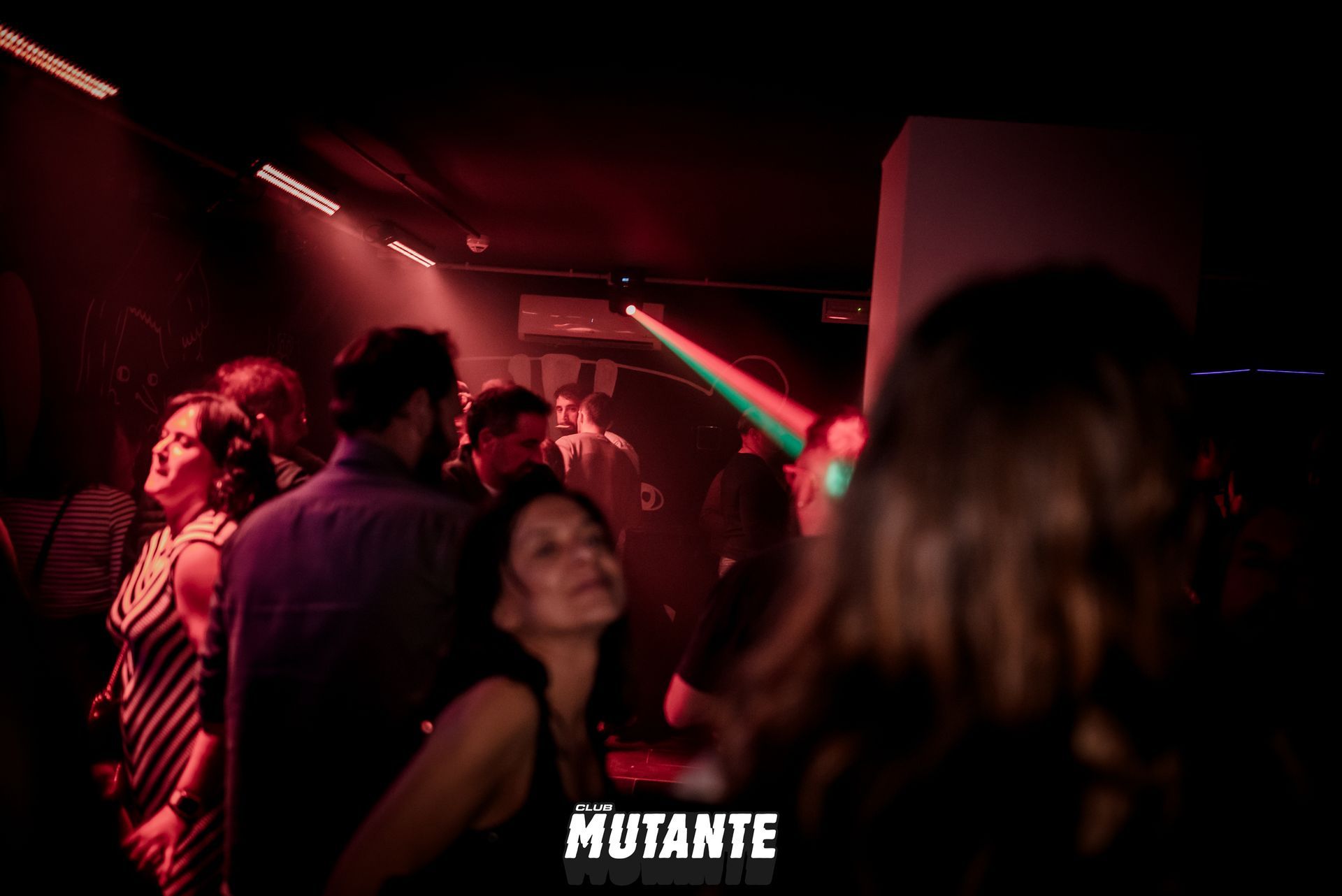 Un grupo de personas está bailando en una habitación oscura con un cartel que dice mutante.