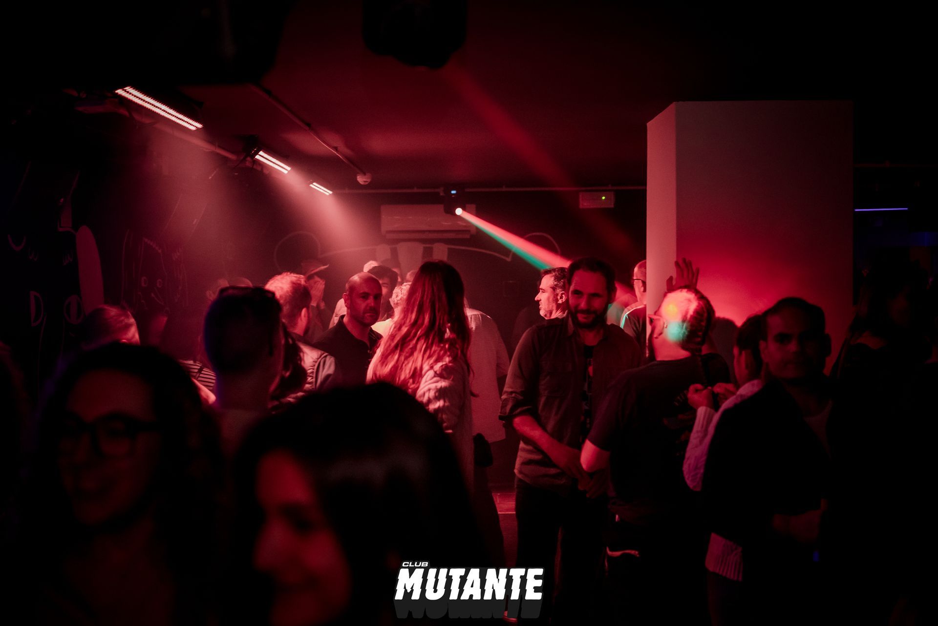 Un grupo de personas está bailando en una habitación oscura con luces rojas.