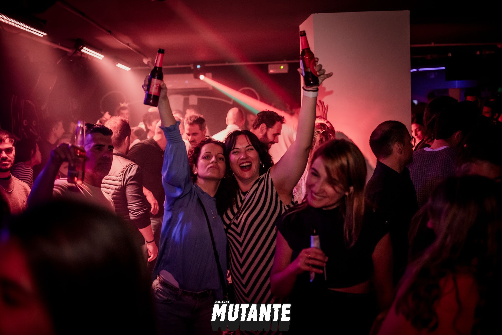 Un grupo de personas baila en un club y sostiene botellas en el aire.