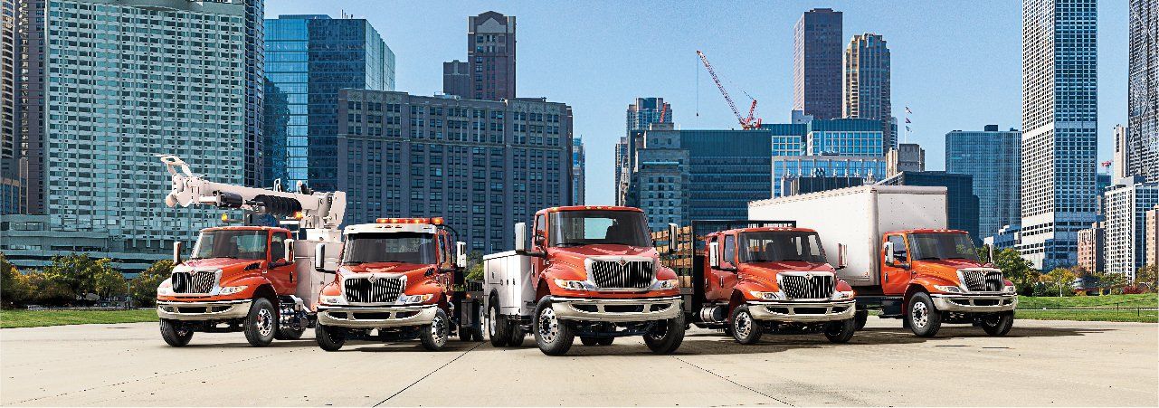 A group of trucks are parked in front of a city skyline.