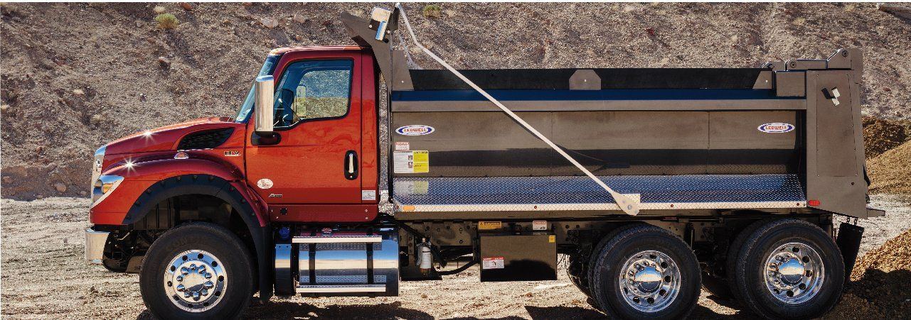 A red dump truck is parked in the middle of a dirt field.