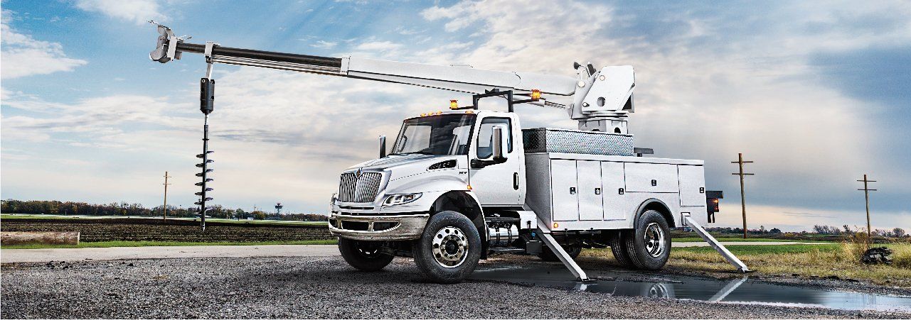 A white utility truck with a crane on top of it is parked on the side of the road.