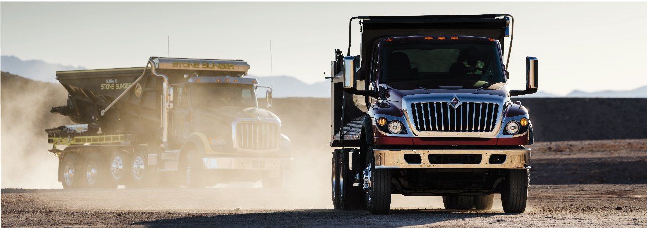 A dump truck is driving down a dirt road next to another truck.