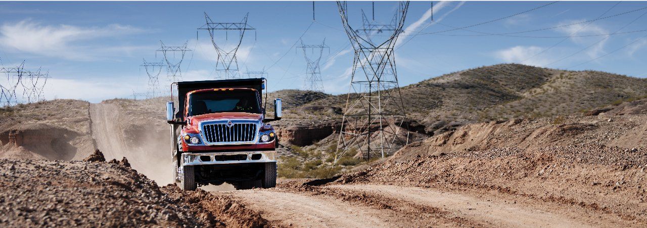 A red dump truck is driving down a dirt road.