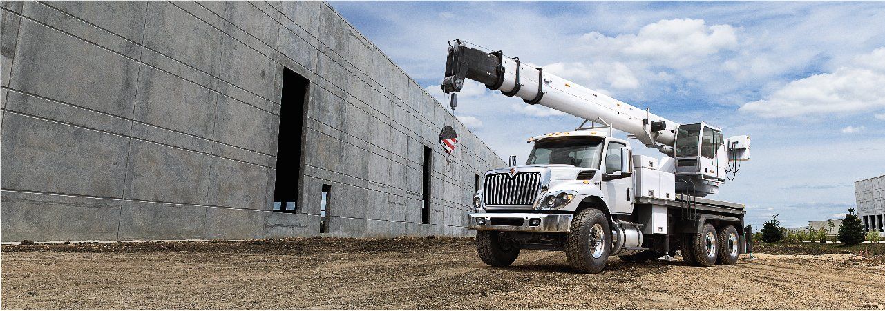 A truck with a crane attached to it is parked in front of a building under construction.