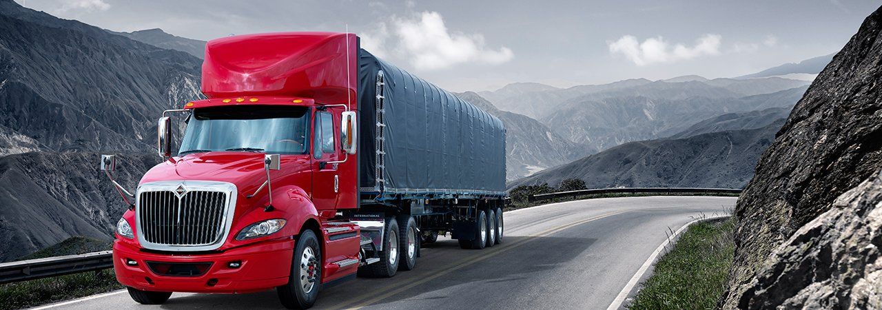 A red semi truck is driving down a mountain road.