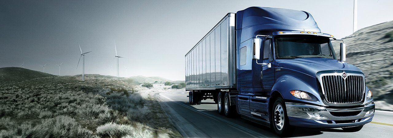 A blue semi truck is driving down a road next to a field.
