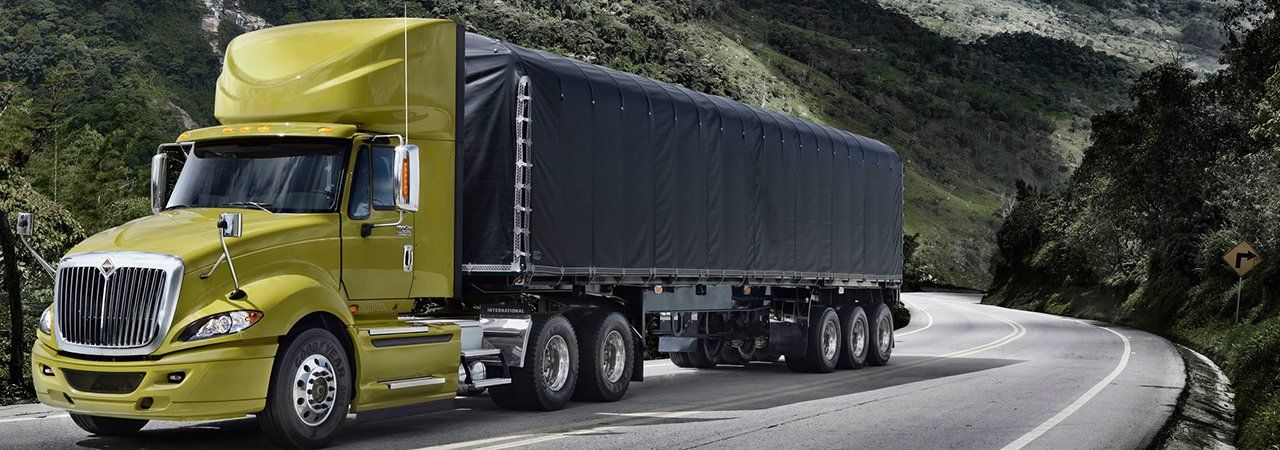 A yellow semi truck is driving down a curvy road.