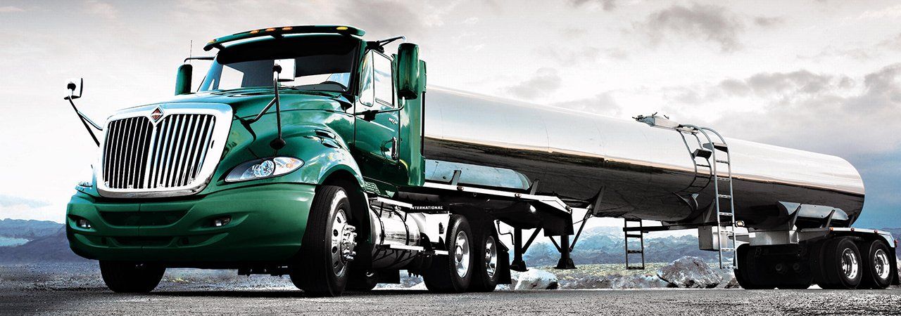 A green semi truck with a tanker trailer is parked on the side of the road.