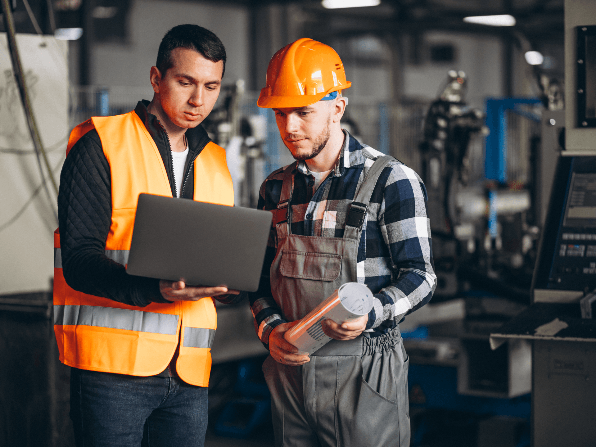 Two men in hard hats are looking at a laptop in a factory.