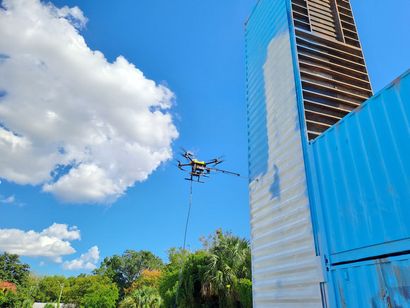 Drone flying near a modern glass building under a blue sky with clouds