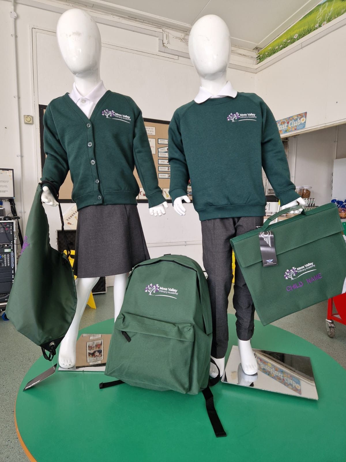 Two mannequins displaying school uniforms and accessories in green, on a green table.