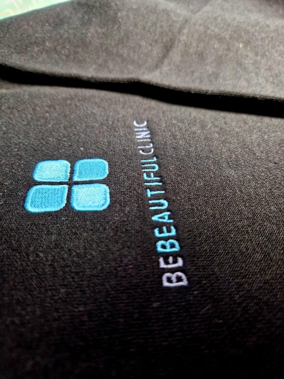 Black fabric with embroidered logo: four light blue squares, text 