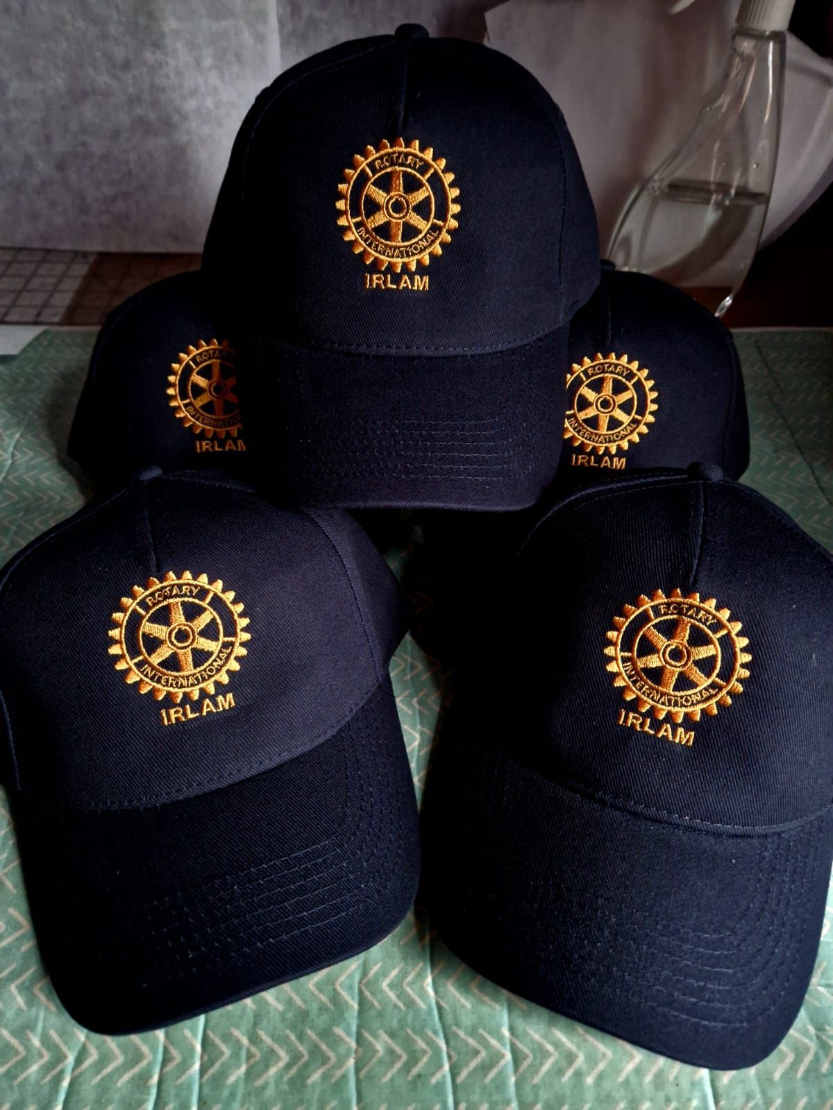Five navy blue baseball caps with gold Rotary Club logos, some arranged on a table.