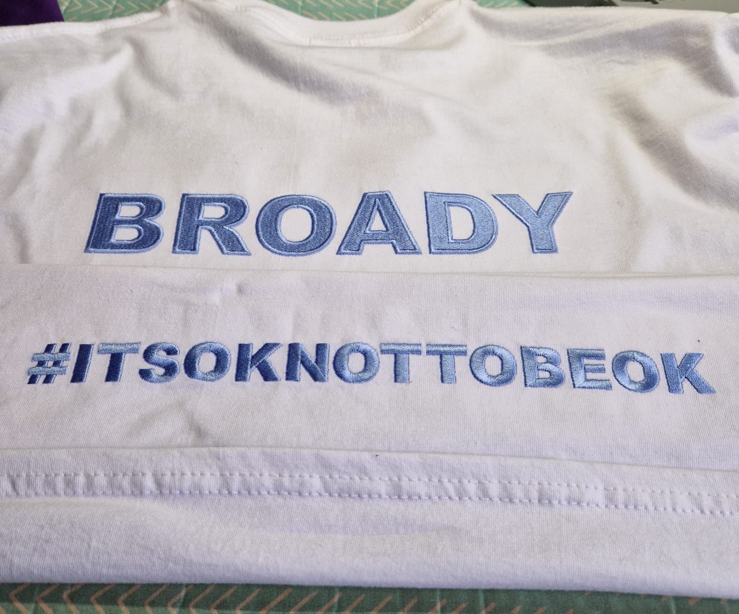 White t-shirt with embroidered blue text: 