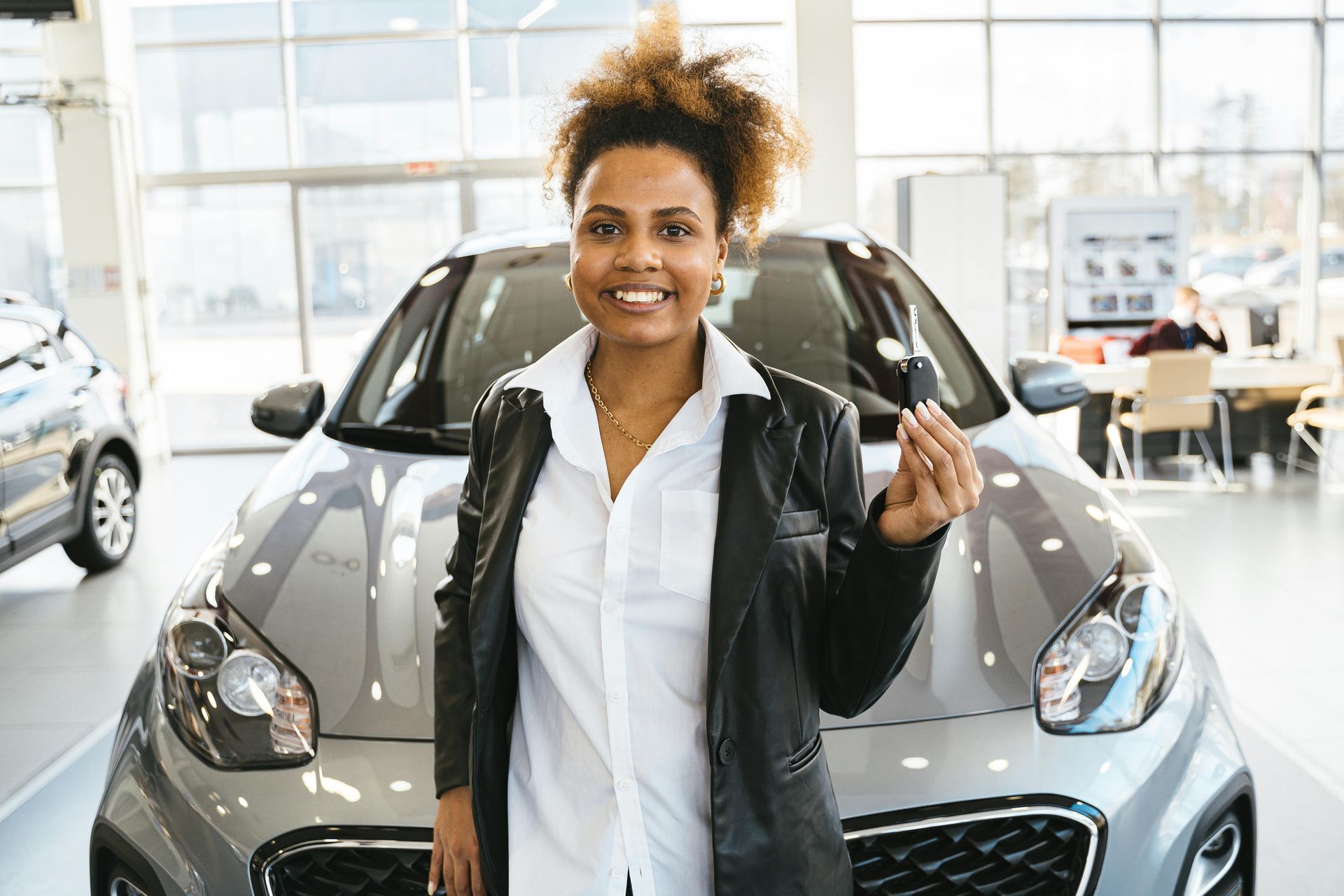 Woman smiling, holding car keys in front of a silver car at a dealership.