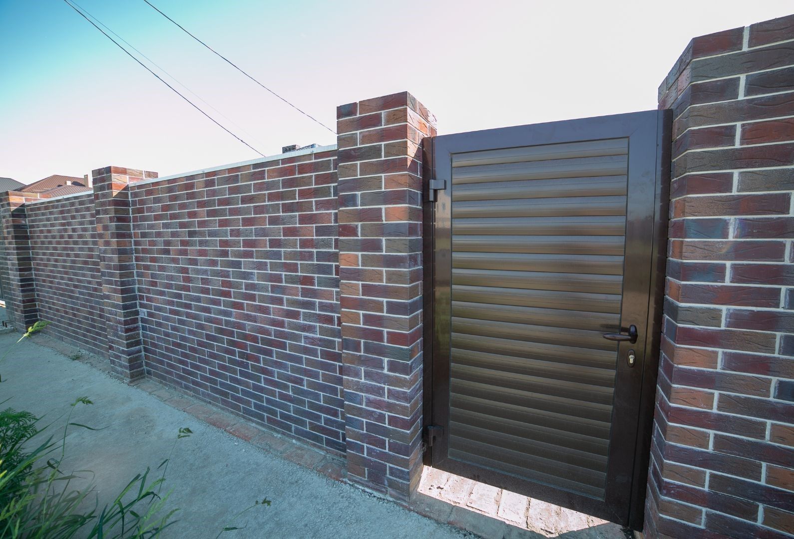 A brick fence with a metal gate in the middle of it.