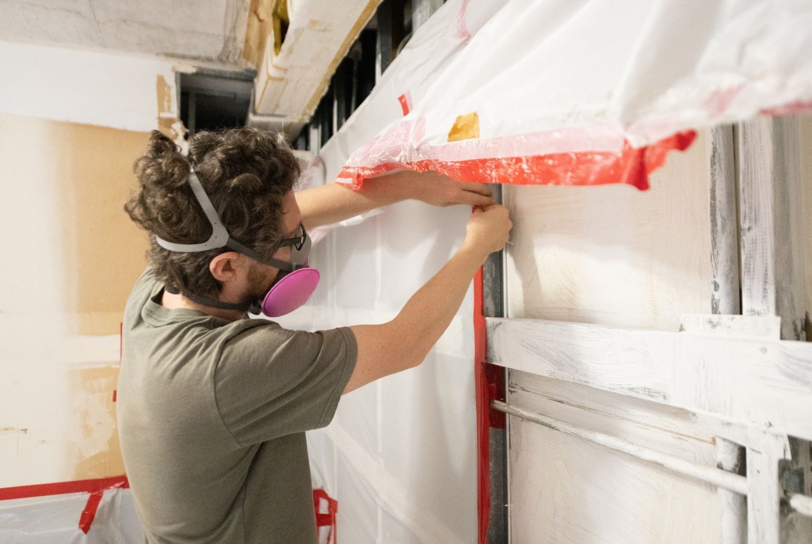 A man wearing a mask and goggles is working on a wall.