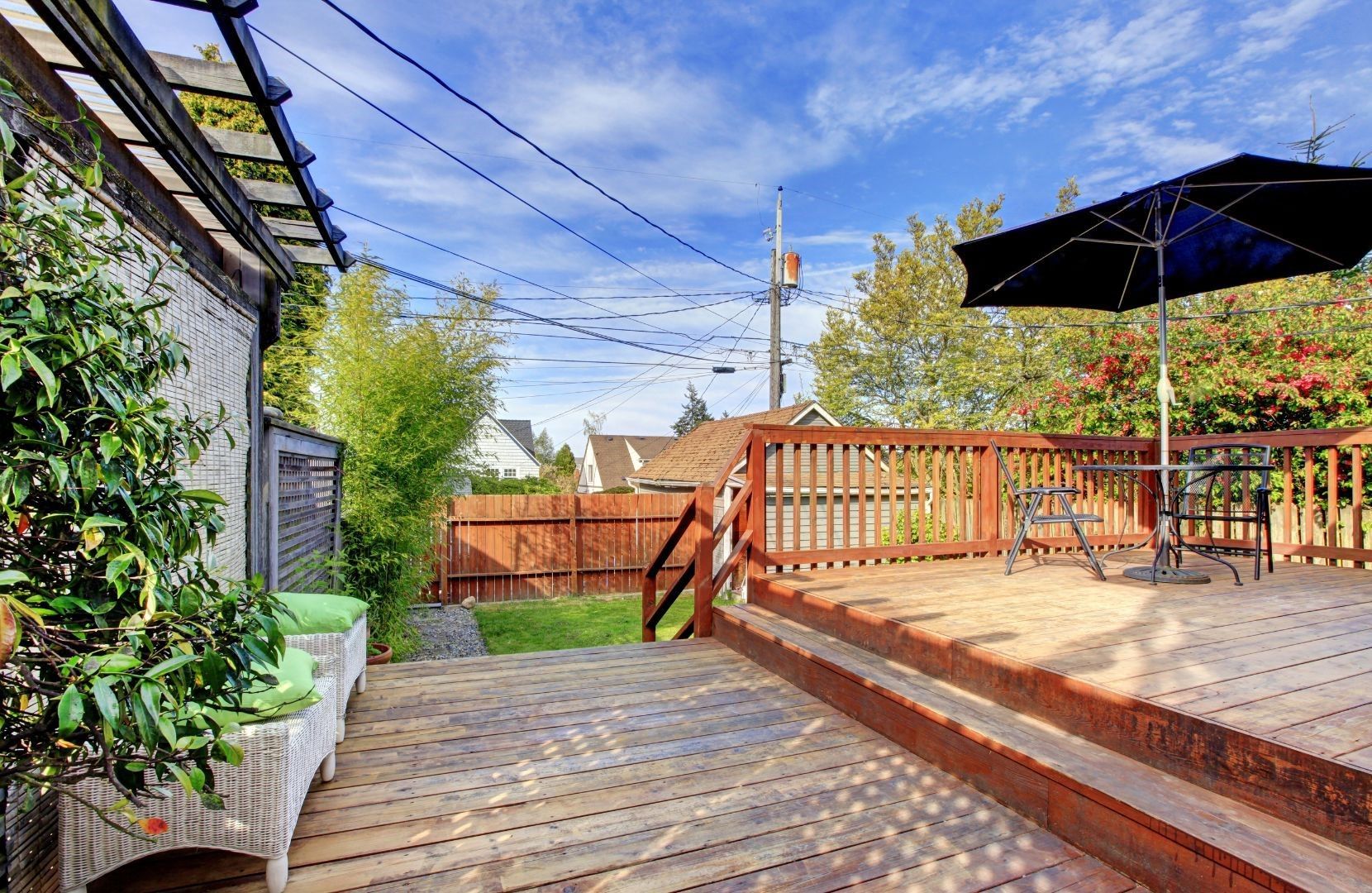 A wooden deck with a black umbrella and chairs on it.