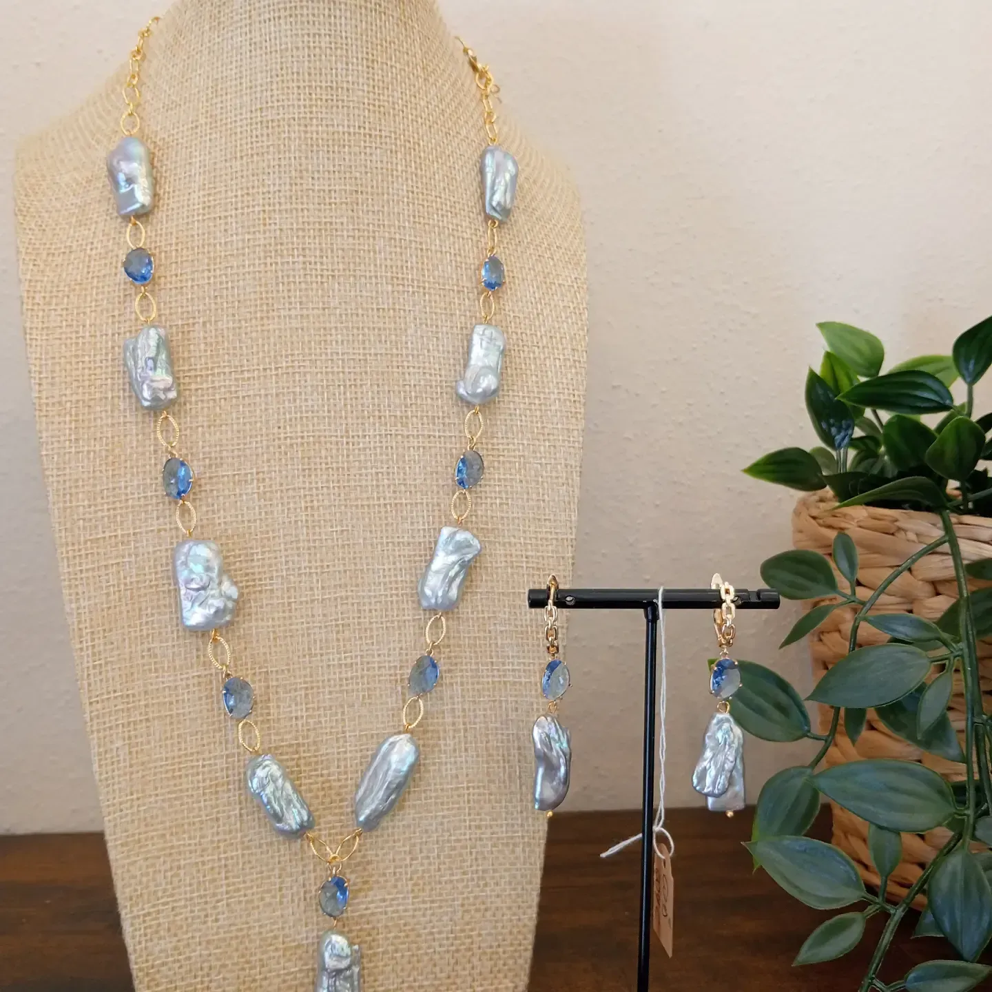 Collana di perline e orecchini abbinati esposti su un busto color beige accanto a una piccola pianta