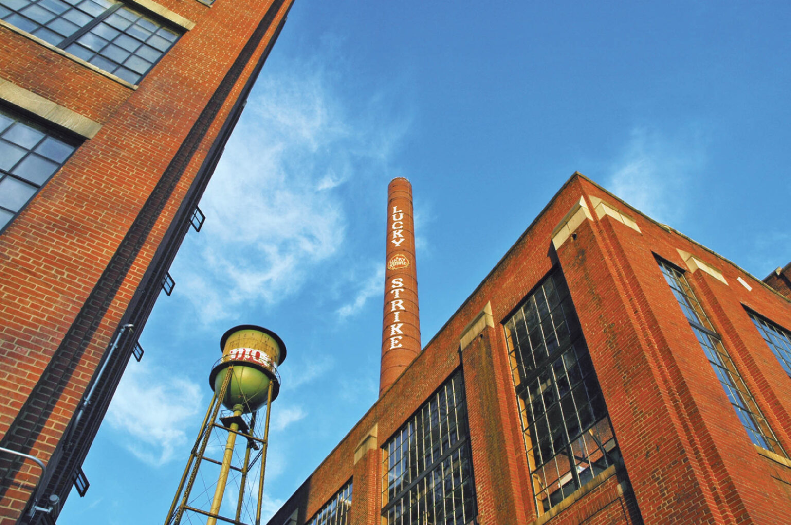 Exterior view of a brick building with a water tower in front of it at The River Lofts at Tobacco Row offers apartments for rent in Richmond, VA.
