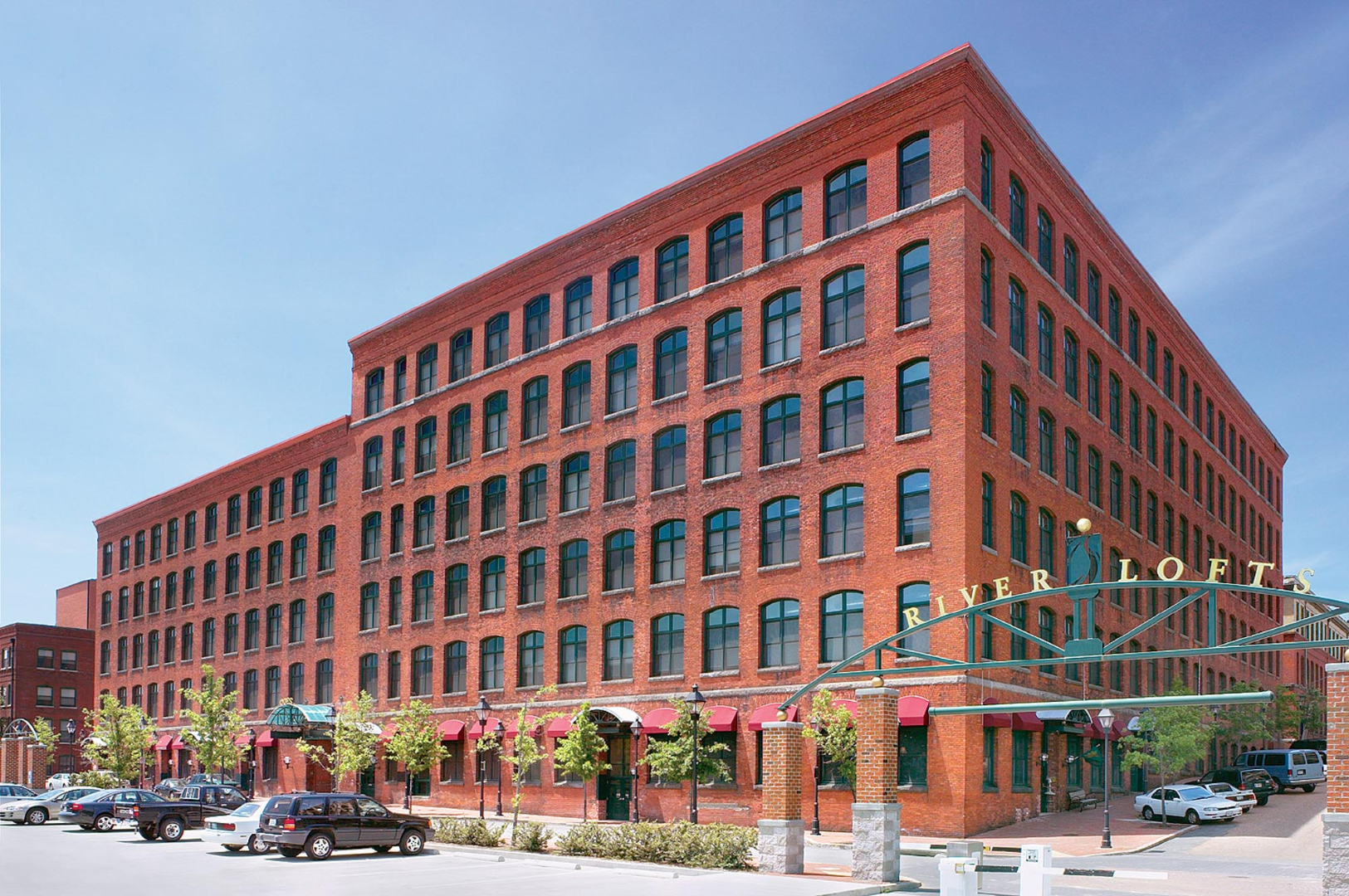A large brick building with a lot of windows and cars parked in front of it at The River Lofts at Tobacco Row offers apartments for rent in Richmond, VA.