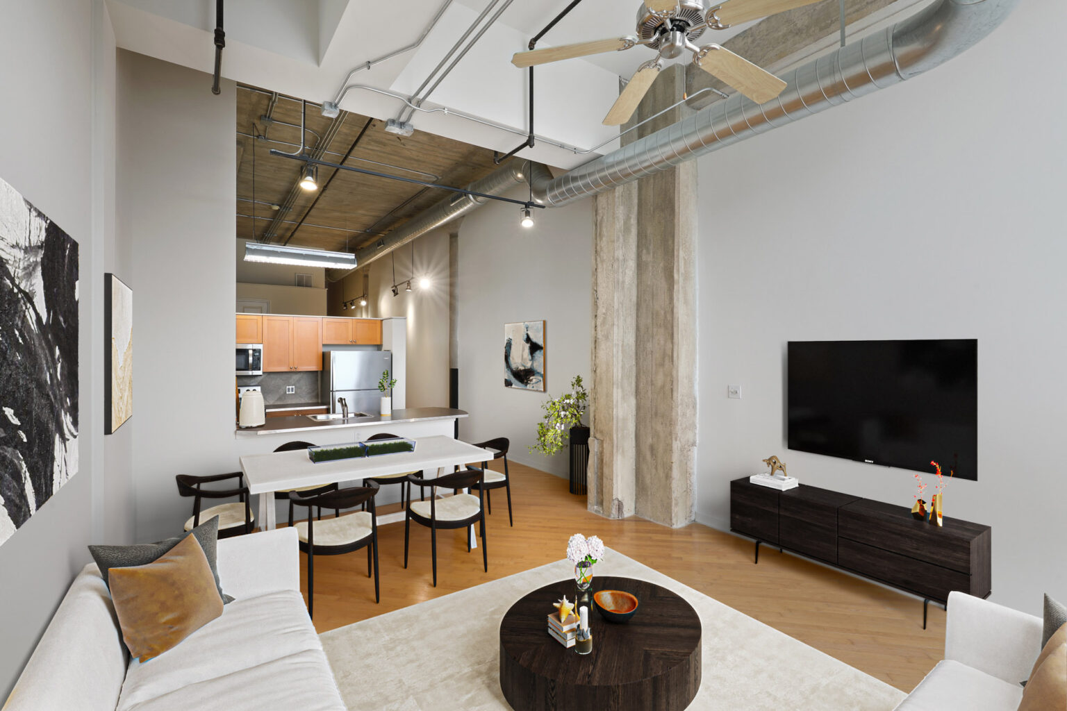 A high-ceiling living room with a couch, coffee table, television, and ceiling fan at The River Lofts at Tobacco Row offers apartments for rent in Richmond, VA.