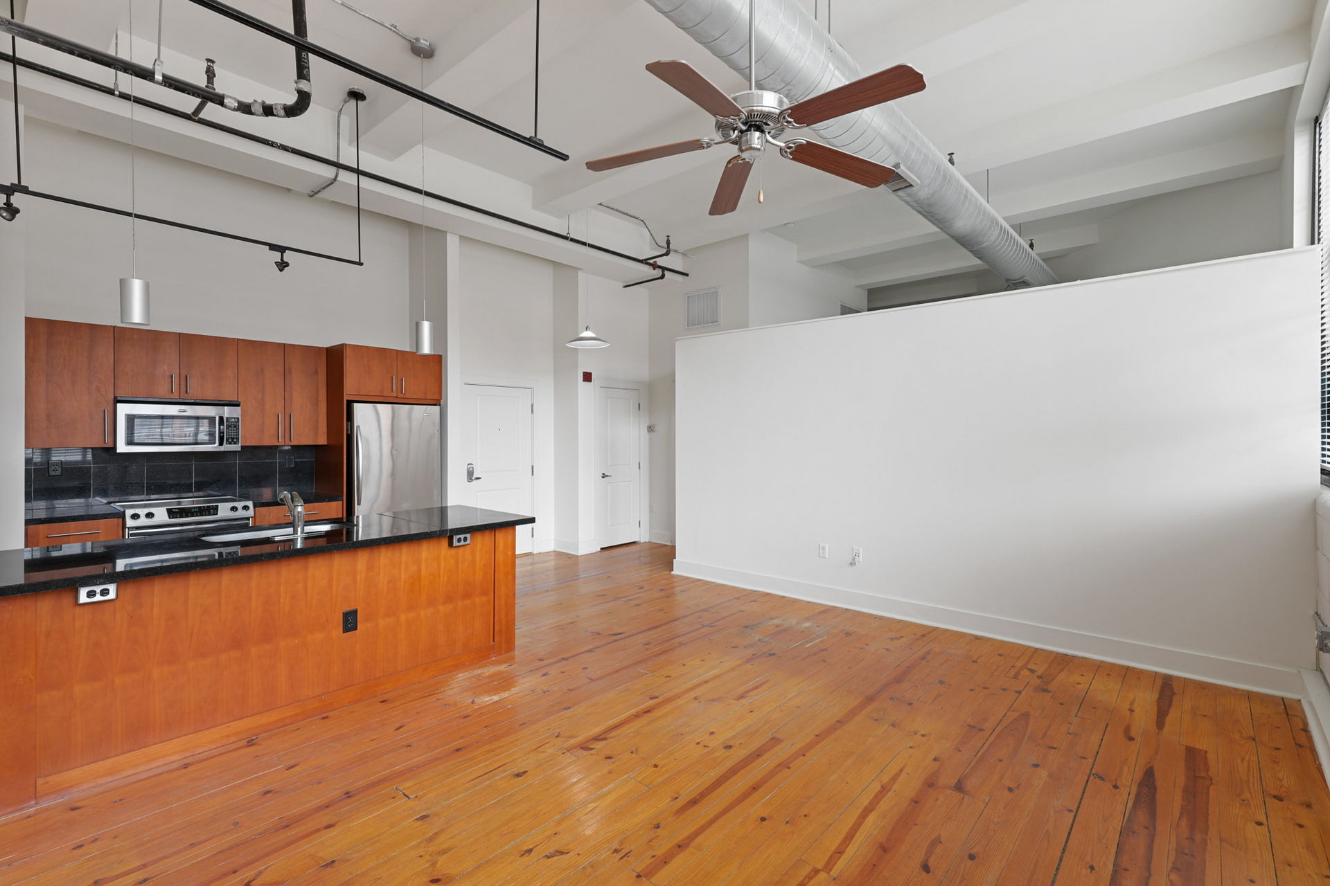 An empty kitchen with wooden floors and a ceiling fan at The River Lofts at Tobacco Row offers apartments for rent in Richmond, VA.