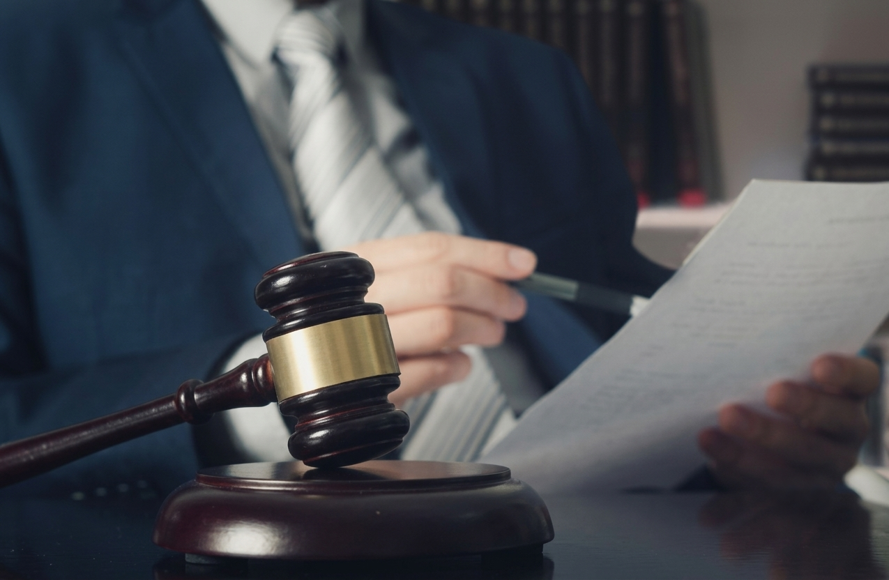 Judge or lawyer in suit reviewing legal documents with wooden gavel on courtroom desk.