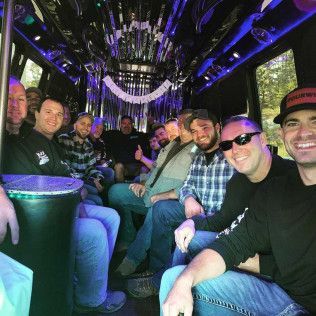 A group of people sitting inside a party bus with blue interior lighting, smiling and looking toward the camera.