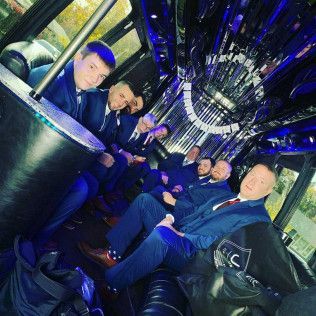 A group of people in formal blue suits sitting inside a brightly lit party limousine.